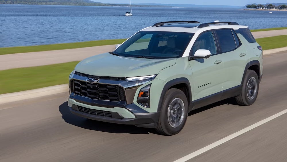 A light green 2026 Chevrolet Equinox SUV driving down a coastal road