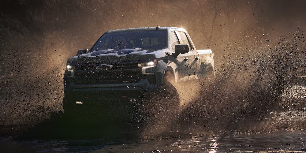 A black 2026 Chevrolet Silverado 1500 pickup truck splashing through muddy water
