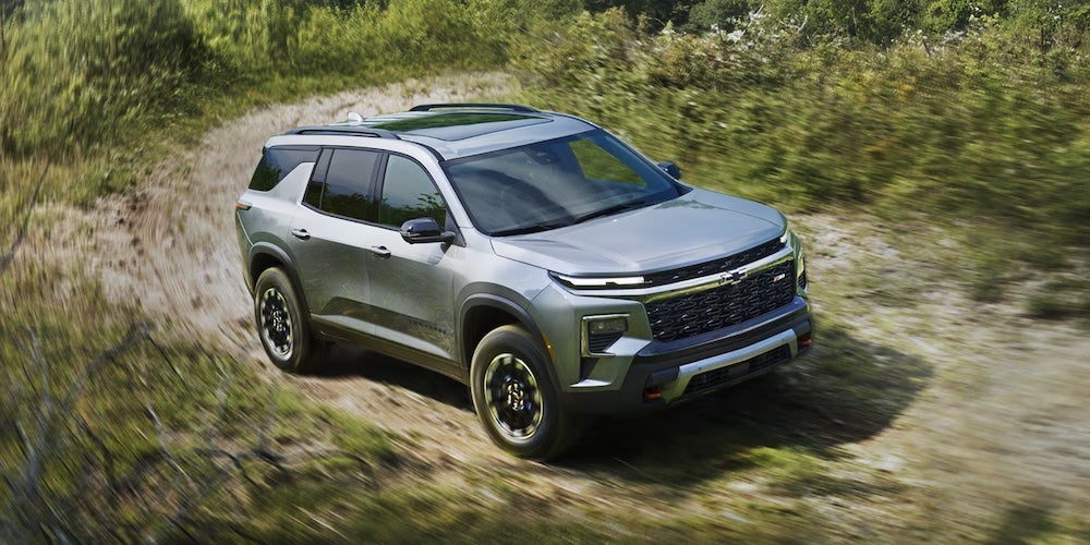 A silver 2026 Chevrolet Traverse SUV driving on a curving dirt road